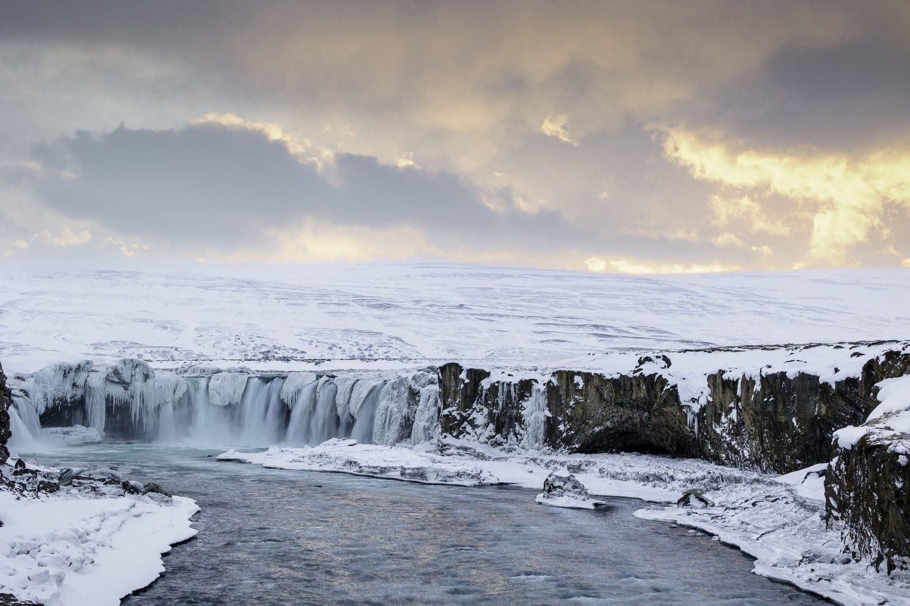 The calving edge of a glacier meeting dark water under flat Arctic light