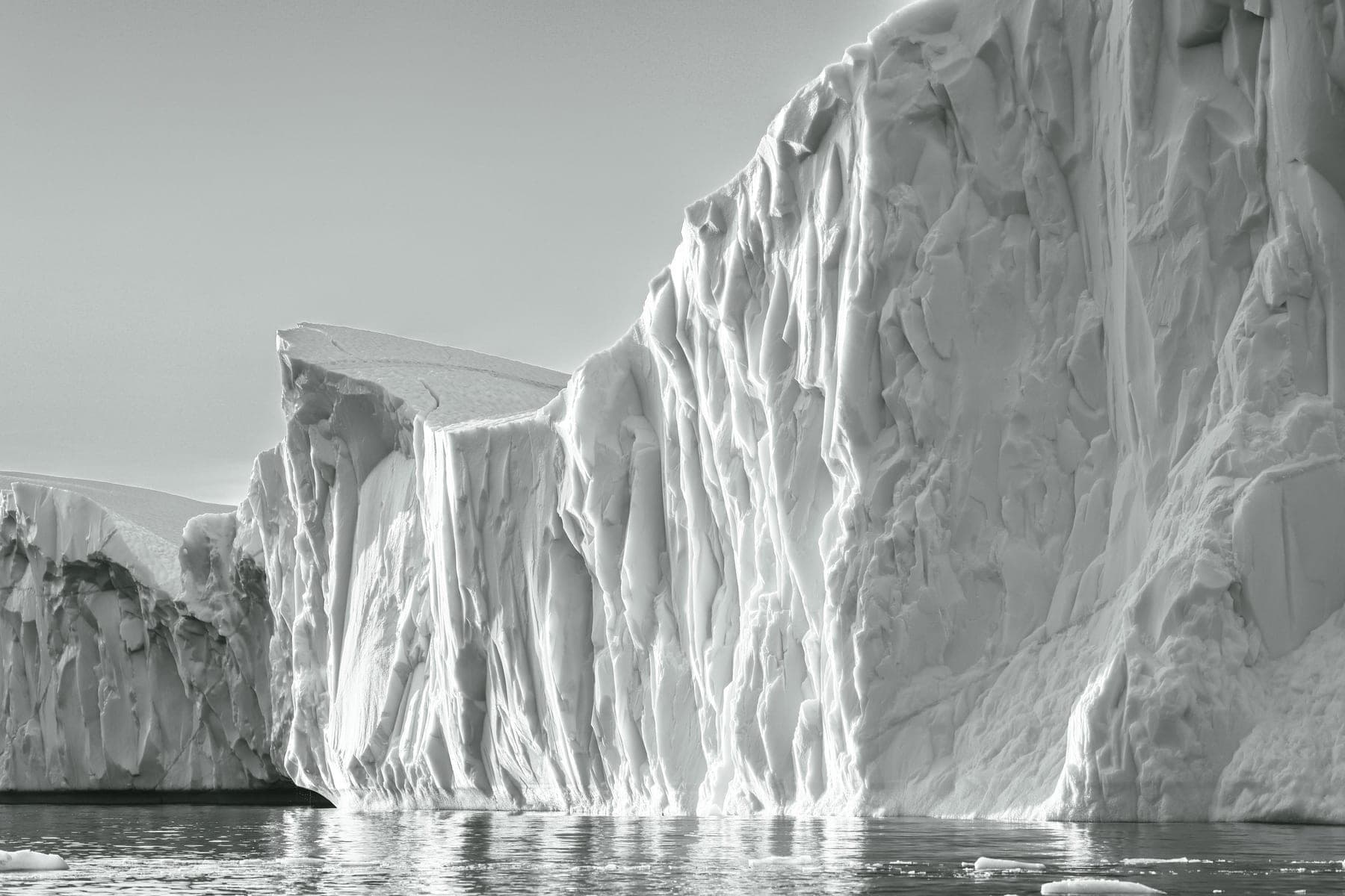 A sunlit white iceberg wall rising above calm water, bright high-key tones