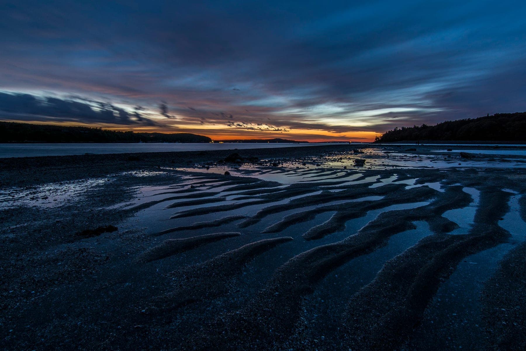Receding surf tracing patterns across a wide black-sand beach at dawn