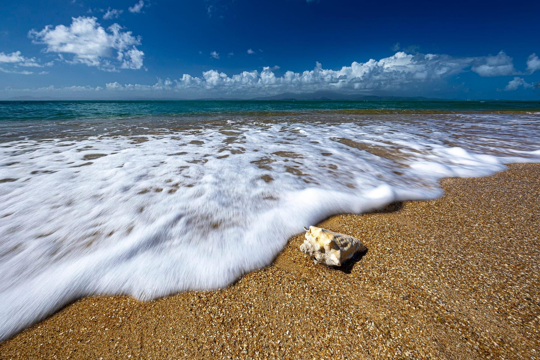 A breaking wave fanning across wet sand at the edge of the surf, long-exposure water