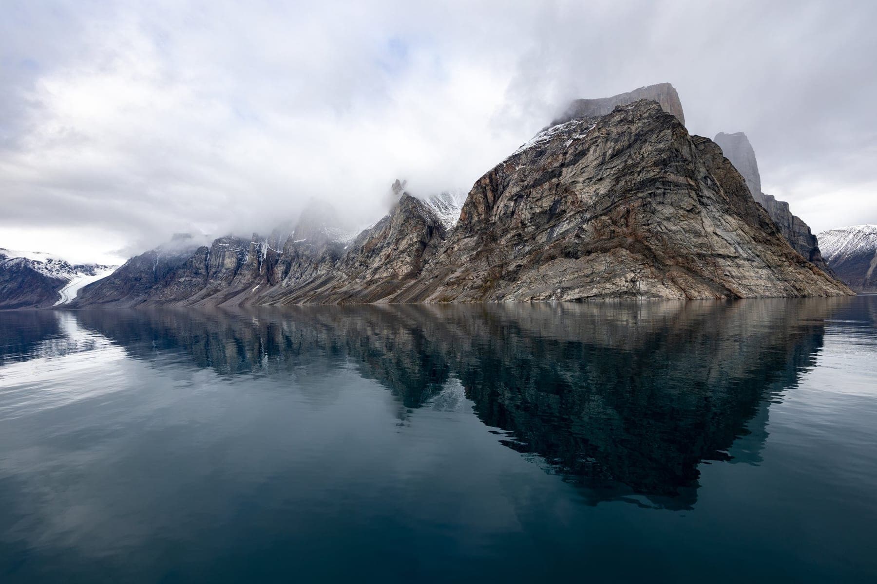 Steep coastal mountains reflected in glassy still water
